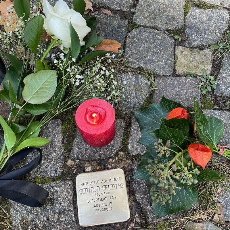 Stolperstein "Gertrud Feiertag" mit Kerze und Blumen